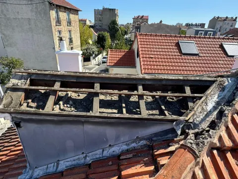 Charpente de toiture fragilisée et noircie par l’humidité autour d’une lucarne, après dépose de la couverture