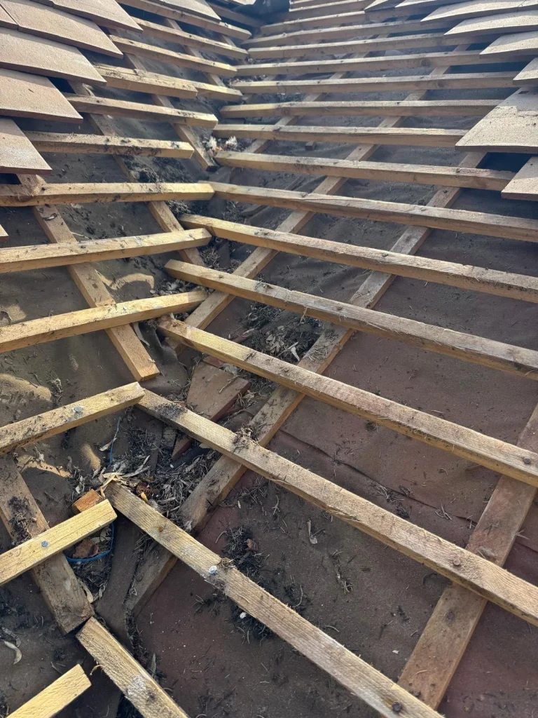 Tuiles et liteaux anciens déposés lors d’une réfection de toiture, débris visibles sur la charpente