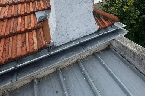 Solin en zinc au pied d’une souche de cheminée, raccordé à une couverture métallique : un point d’entrée d’eau fréquent